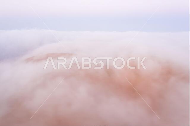 Top of a massive sand dune emerging from a thick cloud of fog after sunrise. Liwa desert, Abu Dhabi, United Arab Emirates.