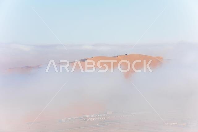 Top of a massive sand dune emerging from a thick cloud of fog after sunrise. Liwa desert, Abu Dhabi, United Arab Emirates.