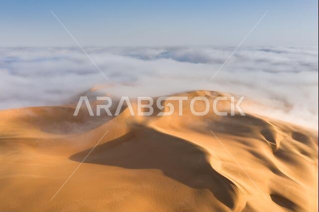 Top of a massive sand dune emerging from a thick cloud of fog after sunrise. Liwa desert, Abu Dhabi, United Arab Emirates.