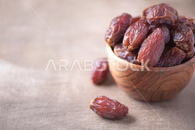 تمر مجفف في وعاء خشبي على خلفية ذات ملمس خشبي. مساحة فارغة. مفهوم الطعام النباتي، والأطعمة فائقة القيمة الغذائية. صورة مقربة لنسيج التمر، مختارة.