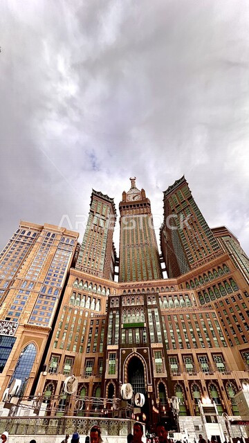 An aesthetic image at an angle from the bottom of the Grand Mosque in Mecca, the royal clock tower building, performing Hajj and Umrah, worship and getting closer to God, Islamic religious landmarks in the Kingdom of Saudi Arabia, a view of clouds and clo