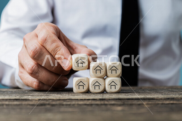 صورة مقربة ليد رجل موظف يعمل في مجال العقارات ، إستشارات عقارية ، شراء و بيع الاملاك العقارية ، مفهوم سوق العقارات ، مكعبات على شكل بيوت ومنازل ، مفهوم الإستثمار العقاري