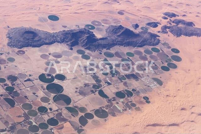 View from the air of round irrigation fields and farms surrounded by sand dunes in the desert in Saudi Arabia