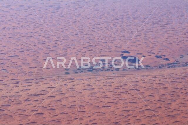 View from the air of round irrigation fields and farms surrounded by sand dunes in the desert in Saudi Arabia