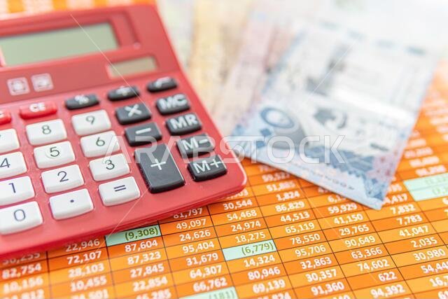 آلة حاسبة حمراء على جدول بيانات مع أوراق نقدية من الريال السعودي