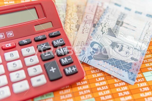 آلة حاسبة حمراء على جدول بيانات مع أوراق نقدية من الريال السعودي