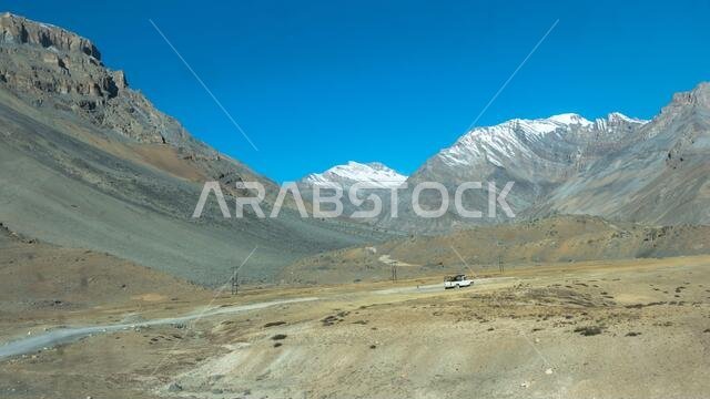 A Tourist car driving far away long mountain hill road trip. Leading to distant peaks Snow covered Desert Himalayas. Mount Everest base camp area. Mys
