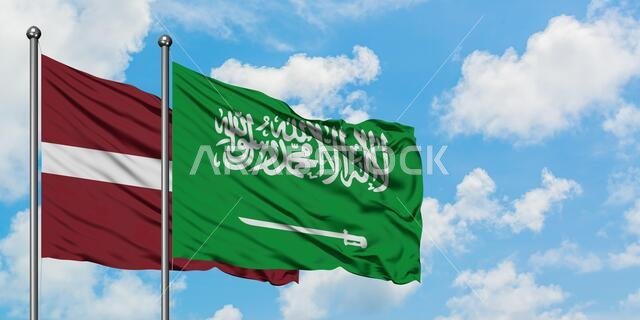 يرفرف علم لاتفيا وعلم المملكة العربية السعودية معاً في مهب الريح أمام سماء زرقاء صافية تتخللها غيوم بيضاء. مفهوم الدبلوماسية، العلاقات الدولية.