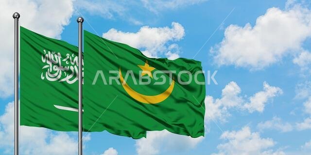 يرفرف علم المملكة العربية السعودية وموريتانيا معاً في مهب الريح أمام سماء زرقاء صافية تتلألأ فيها الغيوم البيضاء. مفهوم الدبلوماسية، العلاقات الدولية.