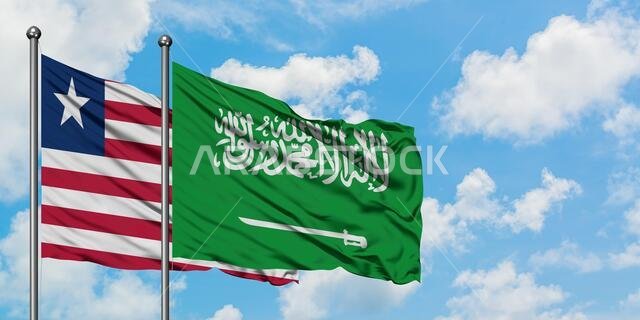يرفرف علما ليبيريا والسعودية معاً في مهب الريح أمام سماء زرقاء صافية تتلألأ فيها الغيوم البيضاء. مفهوم الدبلوماسية، العلاقات الدولية.