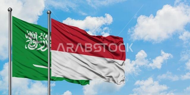 Saudi Arabia and Monaco flag waving in the wind against white cloudy blue sky together. Diplomacy concept, international relations.
