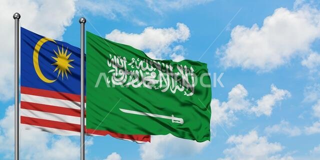 يرفرف علم ماليزيا وعلم المملكة العربية السعودية معاً في مهب الريح أمام سماء زرقاء صافية تتلألأ فيها الغيوم البيضاء. مفهوم الدبلوماسية، العلاقات الدولية.