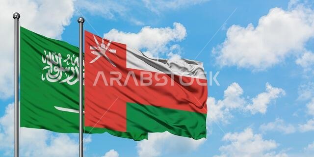 يرفرف علم المملكة العربية السعودية وعلم سلطنة عمان معاً في مهب الريح أمام سماء زرقاء صافية تتخللها غيوم بيضاء. مفهوم الدبلوماسية، العلاقات الدولية.