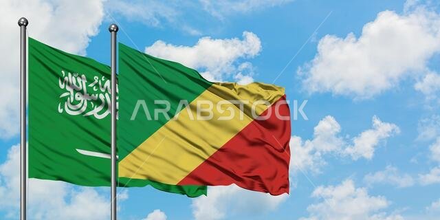 يرفرف علم المملكة العربية السعودية وعلم جمهورية الكونغو في مهب الريح أمام سماء زرقاء صافية تتلألأ فيها الغيوم البيضاء. مفهوم الدبلوماسية، العلاقات الدولية.