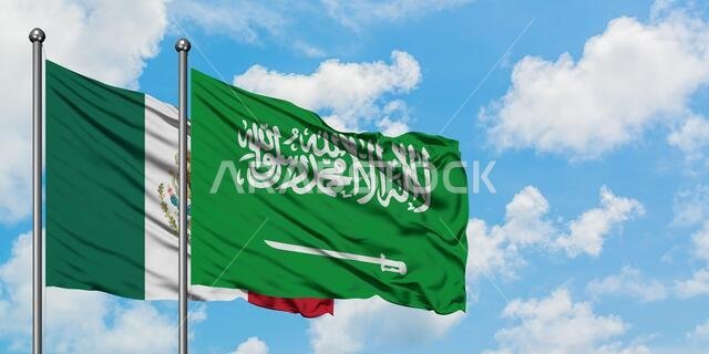 يرفرف علم المكسيك وعلم السعودية معاً في مهب الريح أمام سماء زرقاء ملبدة بالغيوم البيضاء. مفهوم الدبلوماسية، العلاقات الدولية.