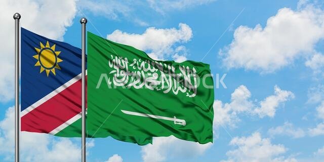 يرفرف علم ناميبيا وعلم المملكة العربية السعودية معاً في مهب الريح أمام سماء زرقاء صافية تتخللها غيوم بيضاء. مفهوم الدبلوماسية، العلاقات الدولية.
