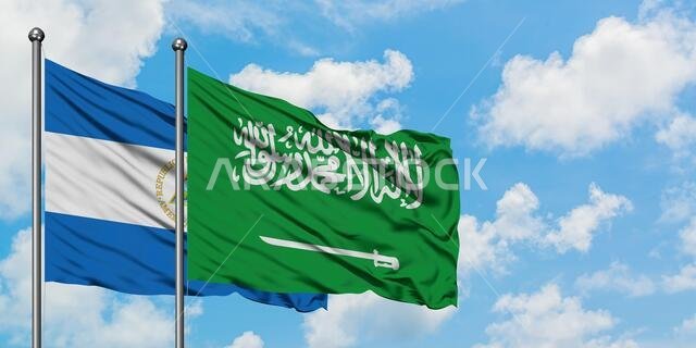 يرفرف علما نيكاراغوا والمملكة العربية السعودية معاً في مهب الريح أمام سماء زرقاء صافية تتلألأ فيها الغيوم البيضاء. مفهوم الدبلوماسية، العلاقات الدولية.