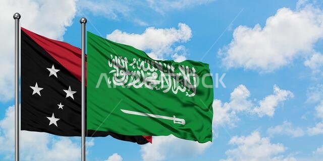 يرفرف علم بابوا غينيا الجديدة وعلم المملكة العربية السعودية معاً في مهب الريح أمام سماء زرقاء ملبدة بالغيوم البيضاء. مفهوم الدبلوماسية، العلاقات الدولية.