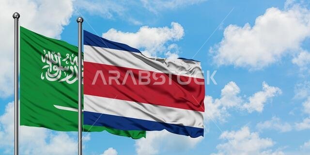 يرفرف علم المملكة العربية السعودية وعلم كوستاريكا معاً في مهب الريح أمام سماء زرقاء صافية تتلألأ فيها الغيوم البيضاء. مفهوم الدبلوماسية، العلاقات الدولية.