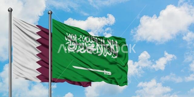 يرفرف علم قطر والسعودية معاً في مهب الريح أمام سماء زرقاء صافية تتلألأ بالغيوم البيضاء. مفهوم الدبلوماسية، العلاقات الدولية.