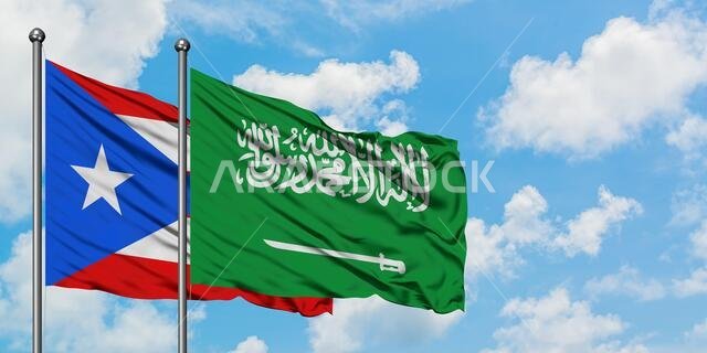 يرفرف علم بورتوريكو وعلم المملكة العربية السعودية معاً في مهب الريح أمام سماء زرقاء ملبدة بالغيوم البيضاء. مفهوم الدبلوماسية، العلاقات الدولية.