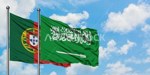 يرفرف علم البرتغال والسعودية معاً في مهب الريح أمام سماء زرقاء صافية تتلألأ بالغيوم البيضاء. مفهوم الدبلوماسية، العلاقات الدولية.