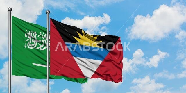يرفرف علم المملكة العربية السعودية وعلم أنتيغوا وبربودا معاً في مهب الريح أمام سماء زرقاء صافية تتلألأ بالغيوم البيضاء. مفهوم الدبلوماسية، العلاقات الدولية.