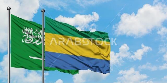 Saudi Arabia and Gabon flag waving in the wind against white cloudy blue sky together. Diplomacy concept, international relations.