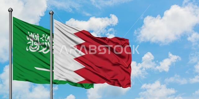 يرفرف علم المملكة العربية السعودية وعلم البحرين معاً في مهب الريح أمام سماء زرقاء صافية تتخللها غيوم بيضاء. مفهوم الدبلوماسية، العلاقات الدولية.