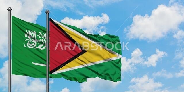 Saudi Arabia and Guyana flag waving in the wind against white cloudy blue sky together. Diplomacy concept, international relations.