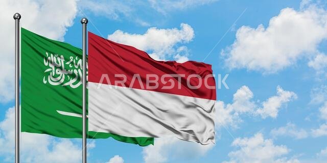 يرفرف علم المملكة العربية السعودية وعلم إندونيسيا معاً في مهب الريح أمام سماء زرقاء صافية تتخللها غيوم بيضاء. مفهوم الدبلوماسية، العلاقات الدولية.