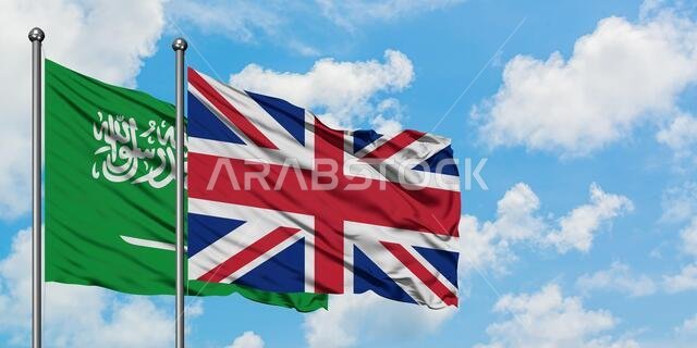 يرفرف علم المملكة العربية السعودية وعلم المملكة المتحدة معاً في مهب الريح أمام سماء زرقاء صافية تتخللها غيوم بيضاء. مفهوم الدبلوماسية، العلاقات الدولية.
