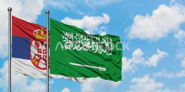 يرفرف علم صربيا والسعودية معاً في مهب الريح أمام سماء زرقاء صافية تتلألأ بالغيوم البيضاء. مفهوم الدبلوماسية، العلاقات الدولية.