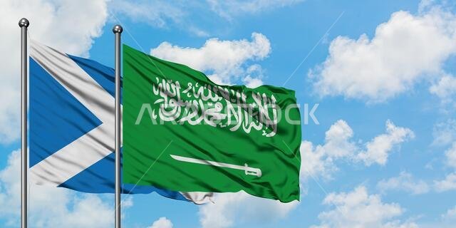 يرفرف علم اسكتلندا وعلم السعودية معاً في مهب الريح أمام سماء زرقاء ملبدة بالغيوم البيضاء. مفهوم الدبلوماسية، العلاقات الدولية.