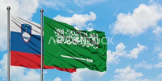 يرفرف علم سلوفينيا والسعودية معاً في مهب الريح أمام سماء زرقاء صافية تتخللها غيوم بيضاء. مفهوم الدبلوماسية، العلاقات الدولية.