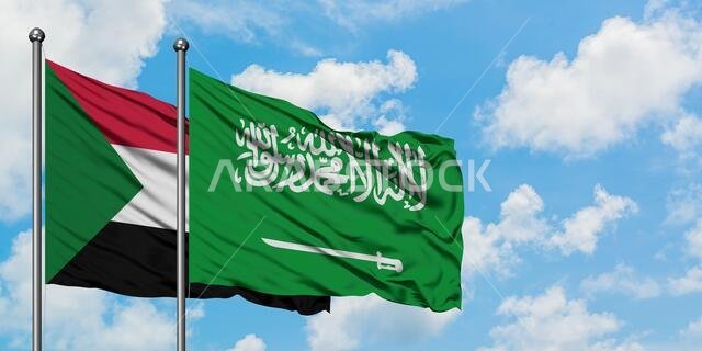 يرفرف علم السودان والسعودية معاً في مهب الريح أمام سماء زرقاء صافية تتلألأ بالغيوم البيضاء. مفهوم الدبلوماسية، العلاقات الدولية.