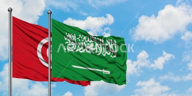 يرفرف علم تونس والسعودية معاً في مهب الريح أمام سماء زرقاء صافية تتلألأ بالغيوم البيضاء. مفهوم الدبلوماسية، العلاقات الدولية.