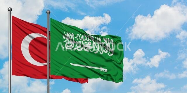 يرفرف علم تركيا والسعودية معاً في مهب الريح أمام سماء زرقاء صافية تتلألأ بالغيوم البيضاء. مفهوم الدبلوماسية، العلاقات الدولية.
