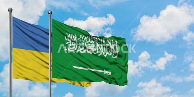 يرفرف علم أوكرانيا وعلم السعودية معاً في مهب الريح أمام سماء زرقاء صافية تتلألأ بالغيوم البيضاء. مفهوم الدبلوماسية، العلاقات الدولية.