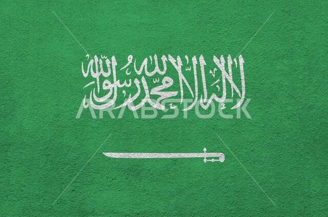 علم المملكة العربية السعودية مرسوم بألوان زاهية على جدار قديم مزخرف بنقوش بارزة، صورة مقربة. لافتة منقوشة على خلفية خشنة.