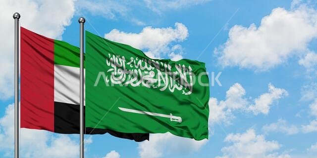 يرفرف علم الإمارات العربية المتحدة والمملكة العربية السعودية معاً في مهب الريح أمام سماء زرقاء صافية تتخللها غيوم بيضاء. مفهوم الدبلوماسية، العلاقات الدولية.