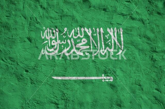 علم المملكة العربية السعودية مرسوم بألوان زاهية على جدار قديم مزخرف بنقوش بارزة، صورة مقربة. لافتة منقوشة على خلفية خشنة.