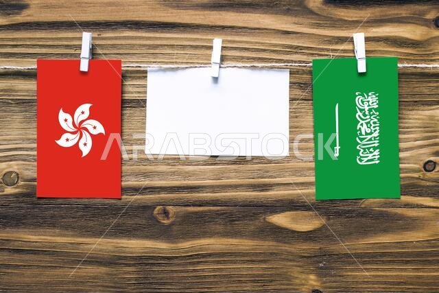 أعلام هونغ كونغ والمملكة العربية السعودية معلقة بحبل بمشابك غسيل، مع مساحة للكتابة على ورقة بيضاء على خلفية خشبية. علاقات دبلوماسية