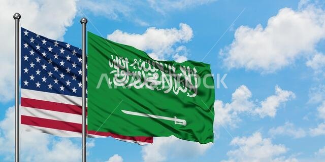 يرفرف علم الولايات المتحدة الأمريكية وعلم المملكة العربية السعودية معاً في مهب الريح أمام سماء زرقاء صافية تتلألأ فيها الغيوم البيضاء. مفهوم الدبلوماسية، العلاقات الدولية.