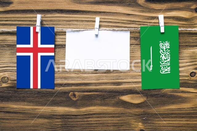 أعلام آيسلندا والمملكة العربية السعودية معلقة بحبل بمشابك غسيل، مع مساحة للكتابة على ورقة بيضاء على خلفية خشبية. علاقات دبلوماسية
