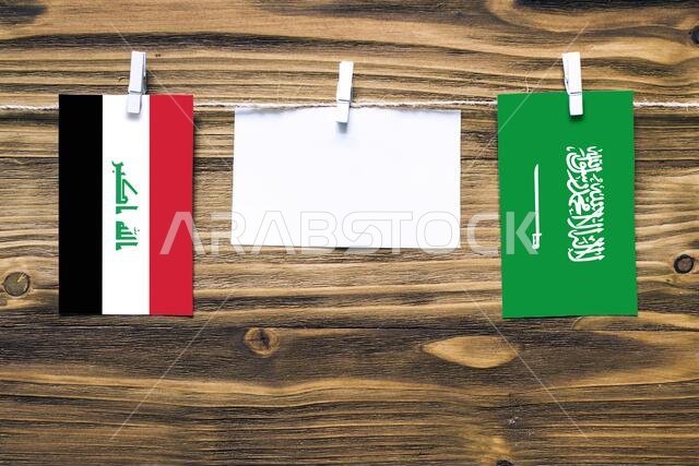 أعلام العراق والسعودية معلقة بحبل بمشابك غسيل، مع مساحة للكتابة على ورقة بيضاء على خلفية خشبية. العلاقات الدبلوماسية