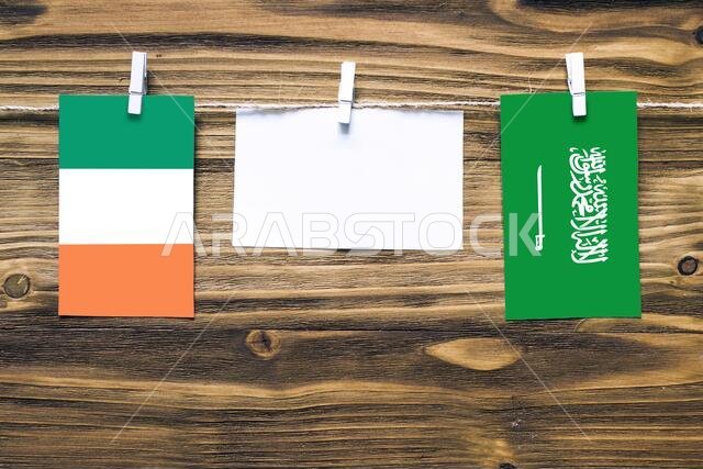 Hanging flags of Ireland and Saudi Arabia attached to rope with clothes pins with copy space on white note paper on wooden background.Diplomatic relat
