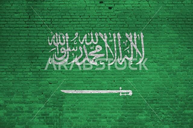 علم المملكة العربية السعودية مرسوم بألوان الطلاء على جدار من الطوب القديم، صورة مقربة. لافتة منقوشة على خلفية جدار كبير من الطوب.
