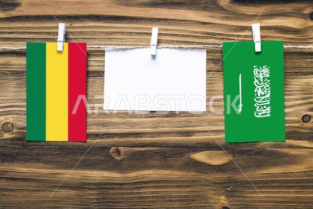 Hanging flags of Bolivia and Saudi Arabia attached to rope with clothes pins with copy space on white note paper on wooden background.Diplomatic relat