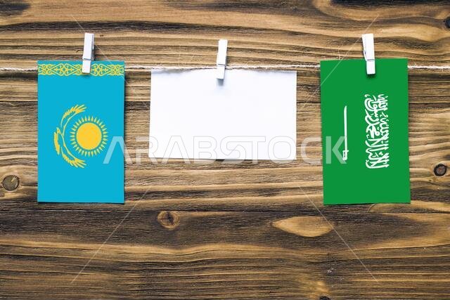 Hanging flags of Kazakhstan and Saudi Arabia attached to rope with clothes pins with copy space on white note paper on wooden background.Diplomatic re